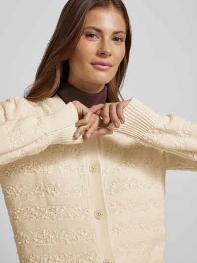 Vrouwenmodel draagt Strickjacke mit Rundhalsausschnitt van Scotch & Soda van katoenmix, regular fit, knoopsluiting, nahaufnahme bovenlichaam.