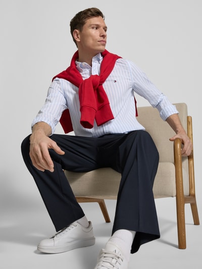 Männermodel trägt Regular Fit Vrijetijdsoverhemd uit katoen-popeline van Tommy Hilfiger met gestreept patroon in wit en lichtblauw, all-over motief, button-downkraag, doorlopende knoopsluiting, logostitching, lange mouw met manchetten, afgeronde rompzoom, puur katoenmateriaal, vooraanzicht bovenlichaam.
