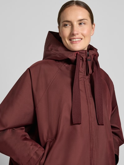 Frauenmodel trägt Relaxed Fit Mantel mit Kapuze Modell 'PURE' von g-lab in dunklem Bordeauxrot, glatte Struktur, Nahaufnahme Oberkörper. Damen Mantel mit Tunnelzug und Eingrifftaschen, Rückenlänge 69 cm, Schulterbreite 45 cm, Brustweite 88 cm, Ärmellänge 60 cm.