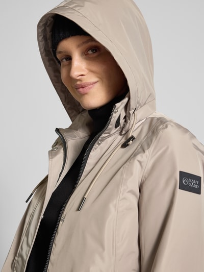 Frauenmodel trägt Regular Fit Mantel mit Logo-Applikation von NAUTGÅRD in Beige, Kapuze mit Tunnelzug, Eingrifftaschen, Nahaufnahme Oberkörper. Rückenlänge 88 cm, Schulterbreite 37 cm, Brustweite 48 cm, Ärmellänge 63 cm.