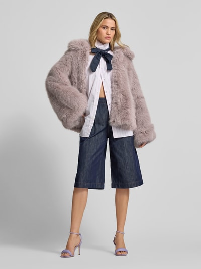 Modelka nosi Flared Jacke aus Kunstfell od ROTATE, jasnofioletowe sztuczne futro, prosta forma, szerokie rękawy, z podszewką z wiskozy, długość tyłu 60 cm, szerokość w rozmiarze 36: 39 cm, długość rękawa 66 cm, widok całej sylwetki z przodu.