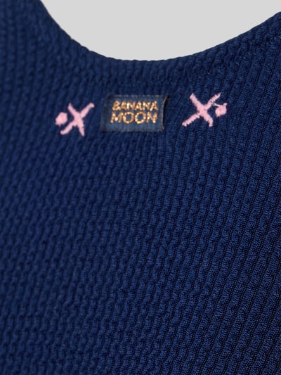 Frauenmodel trägt Badeanzug mit Label-Detail Modell 'BELMAR' von Banana Moon in Marineblau, Struktur mit Material-Mix, Nahaufnahme Oberkörper.