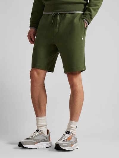 Männermodel trägt Regular Fit Sweatshorts aus Baumwoll-Mix von Polo Ralph Lauren in unifarbenem Grün mit elastischem Bund und Logo-Stitching, Ganzkörperansicht von vorne.