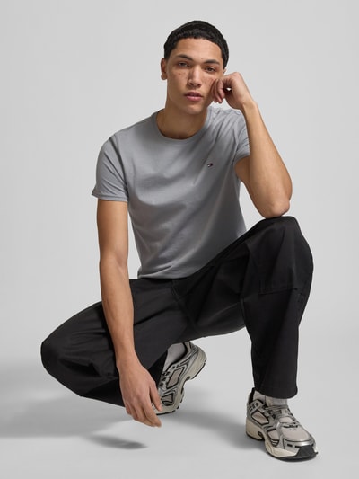 Männermodel trägt Regular Fit T-Shirt aus reiner Baumwolle von Tommy Jeans, Optik: unifarben, Logo-Stitching, Kurzarm, Ganzkörperansicht von vorne.