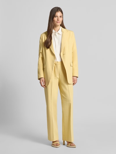 Frauenmodel trägt Wide Fit Stoffhose aus Lyocell-Mix Modell 'Edie' von Scotch & Soda in Gelb mit Bügelfalten, Ganzkörperansicht von vorne.