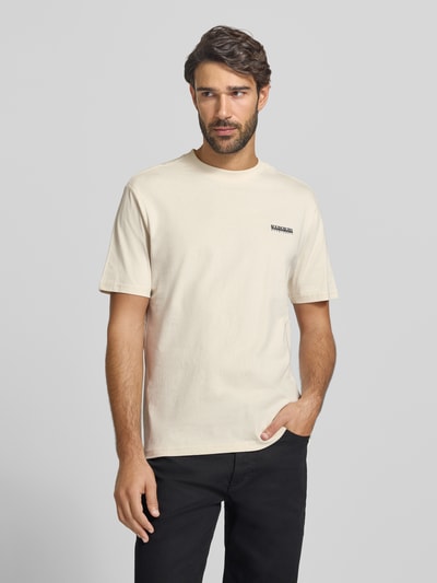 Męski model nosi T-Shirt mit Logo und Rundhalsausschnitt von Napapijri, bawełna z domieszką elastanu, krój regular fit, jasny beż, logo, widok całej sylwetki z przodu, długość tyłu w rozmiarze M: 63 cm.