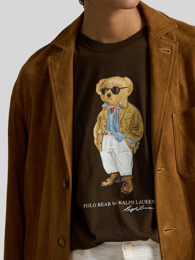 Männermodel trägt Regular Fit T-Shirt aus reiner Baumwolle von Polo Ralph Lauren in Braun, Motiv-Print und Label-Schriftzug, Nahaufnahme Oberkörper.