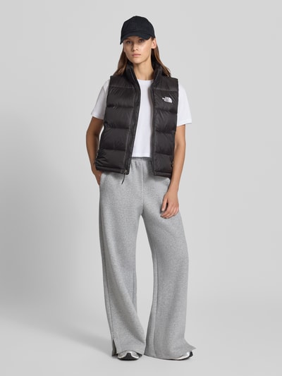 Frauenmodel trägt Steppweste mit Label-Stitching Modell 'HYDRENALITE DOWN A-LINE' von The North Face, schwarze Farbe, Reißverschluss, Regular Fit, kombinierbar mit Basic-Shirt und grauen, weiten Hosen, Ganzkörperansicht von vorne.