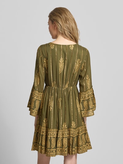 Frauenmodel trägt Minikleid aus Viskose-Mix mit Schnürung von Apricot in Olivgrün mit goldfarbenem Muster, A-Linie, Trompetenärmel, Rückenlänge bei Größe S 83 cm, Brustweite 35 cm, Ärmellänge 50 cm, Ganzkörperansicht Rückansicht.