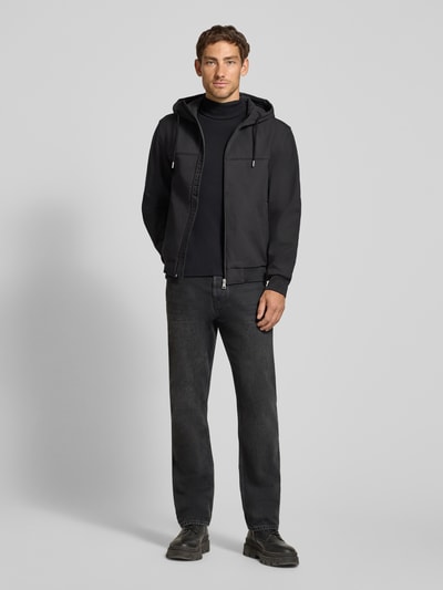 Männermodel trägt Regular Fit Funktionsjacke mit Kapuze von Tom Tailor Denim in Schwarz, dezentes Design, glatte Textur, Ganzkörperansicht von vorne, Herren Funktionsjacke von Tom Tailor Denim.