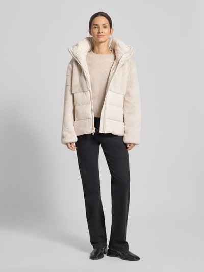 Modelka nosi Steppjacke mit Kunstfellbesatz Modell 'FANEVIL' od Blauer Usa, krój regular fit, kolor jasny beż, całkowity widok z przodu. Długość tyłu 64 cm, szerokość ramion 43 cm, szerokość w rozmiarze S 55 cm, długość rękawa 62 cm, stójka, dwustronny zamek, miękka tekstura.