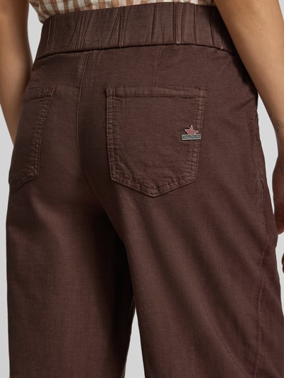 Frauenmodel trägt Culotte aus Viskose-Mix mit Knopfverschluss Modell 'Martinique' von Buena Vista, brauner Baumwoll-Viskose-Mix, strukturierter Stoff, Gesäßtasche mit Label und elastischer Bund, Kontext: Loose-Fit, französische Eingrifftaschen, Bundweite 39 cm, Innenbeinlänge 64 cm bei Größe S, Detailaufnahme Rückansicht.