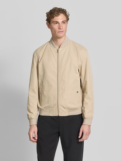 Męski model nosi Regular Fit College-Jacke mit Label-Applikation Modell 'COMBER-262' von BOSS, efekt: jednolity kolor, krój regular fit, kołnierz college, zamek błyskawiczny, aplikacja z metką, długi rękaw, wpuszczane kieszenie boczne, kieszeń napoleonka, wykończenie materiału: splot twill, beżowa kurtka, czarne spodnie, Ganzkörperansicht von vorne