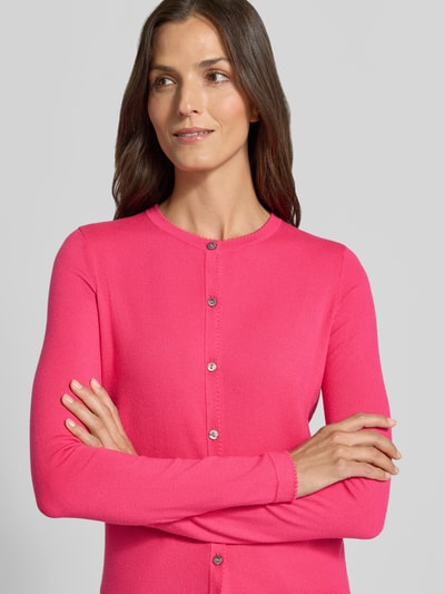 Vrouwenmodel draagt Regular Fit gebreid jack uit viscosemix met geschulpte zoom van Christian Berg Woman, lange mouw, knoopsluiting, ribboorden, ruglengte maat S 56 cm, mouwlengte maat S 61 cm, knalroze, simpele textuur, bovenlichaam close-up.