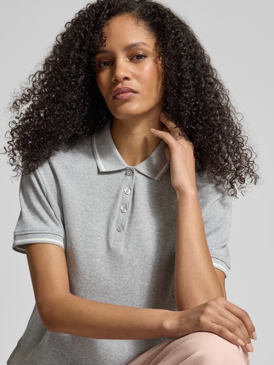 Modelka nosi Regular Fit Poloshirt aus Baumwolle von Jake*s Casual, szara koszulka polo z bawełny, kołnierzyk polo, krój regular fit, elastyczne zakończenia rękawów, długość tyłu w rozmiarze M: 54 cm, zbliżenie na górną część ciała.