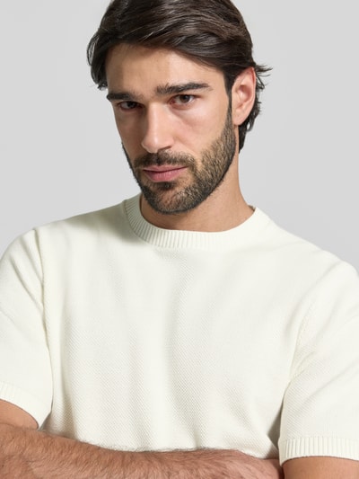 Męski model nosi Regular Fit T-Shirt aus reiner Baumwolle od MCNEAL, prążkowana stójka, prążkowane wykończenia, fakturowany wzór, kremowy kolor, długość tyłu 71 cm, długość rękawa 27 cm, zbliżenie na górną część ciała.