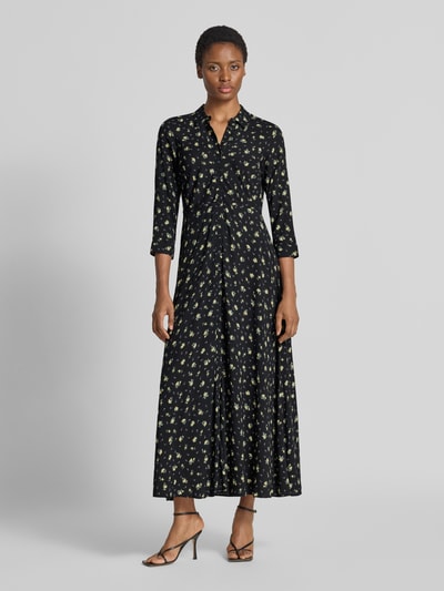 Frauenmodel trägt Maxikleid aus reiner Viskose Modell 'Savanna' von YAS mit floralem Allover-Print, taillierte Passform, 3/4-Arm, dunkle Grundfarbe, weicher Stoff, Ganzkörperansicht von vorne.
