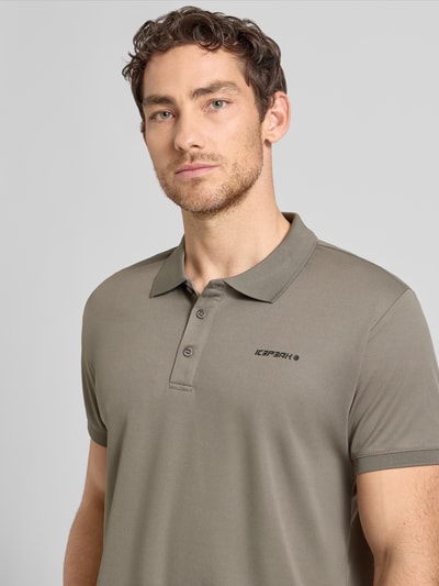 Męski model nosi Regular Fit Poloshirt mit Logo-Print Modell 'BELLMONT' od Icepeak, kolor khaki, krój regular fit, kołnierzyk polo, krótki rękaw, długość tyłu w rozmiarze M: 73 cm, nadruk z logo, zbliżenie na górną część ciała.