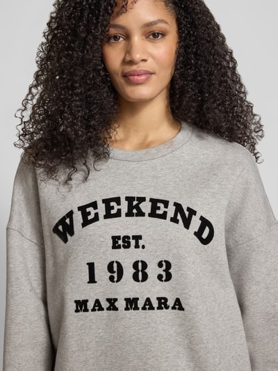Kobiece modelka ma na sobie Oversized Sweatshirt aus reiner Baumwolle od Weekend Max Mara, szary, jednolity, dzianina, nadruk, dekolt okrągły, długie rękawy, elastyczne wykończenia, widoczne kieszenie po bokach; zdjęcie w ujęciu z przodu, zbliżenie na górną część ciała.