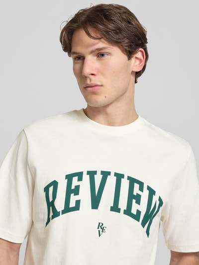 Męski model nosi T-Shirt mit Label-Print und Rundhalsausschnitt od REVIEW, biała bawełna, krój regular fit, długość tyłu 69 cm, nahaufnahme górnej części ciała.