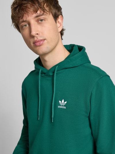 Männermodel trägt Hoodie mit Kapuze von adidas Originals in Grün, Baumwoll-Mix, lockerer Schnitt, Nahaufnahme Oberkörper.