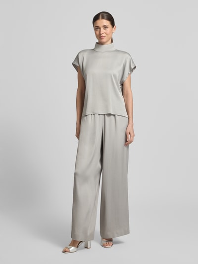 Kobieta nosi Blusenshirt mit Stehkragen Modell 'ALARIA' von Drykorn, mieszanka materiałów z dodatkiem streczu, krój regular fit, długość tyłu w rozmiarze 36: 59 cm, kolor jasnoszary, gładka tekstura, całkowity widok od przodu.