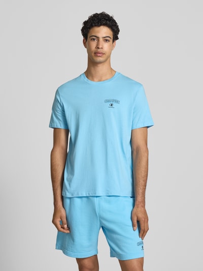Männermodel trägt T-Shirt mit Logo und Rundhalsausschnitt von CHAMPION in Hellblau aus Reine Baumwolle, Regular-Fit, Ganzkörperansicht von vorne. Rückenlänge bei Größe M: 61 cm.