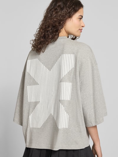 Modelka kobieca ma na sobie Oversized T-Shirt mit Rundhalsausschnitt von Karo Kauer z bawełny, krój oversized, krótki, nadruk z logo, okrągły dekolt, długość tyłu w rozmiarze S: 61 cm, widok całej sylwetki z tyłu.
