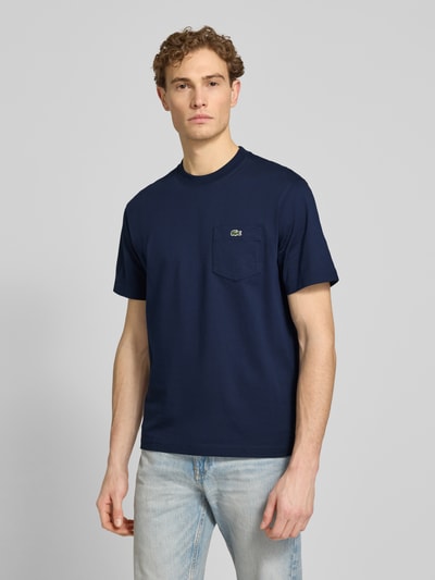 Männermodel trägt Regular Fit T-Shirt aus reiner Baumwolle von Lacoste in Optik: Unifarben mit Logo-Stitching, Label-Print, Rundhals, Ganzkörperansicht von vorne.