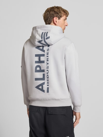 Männermodel trägt Hoodie mit Känguru-Tasche von Alpha Industries in Hellgrau mit Label-Print, Baumwoll-Mix, Ganzkörperansicht Rückansicht.