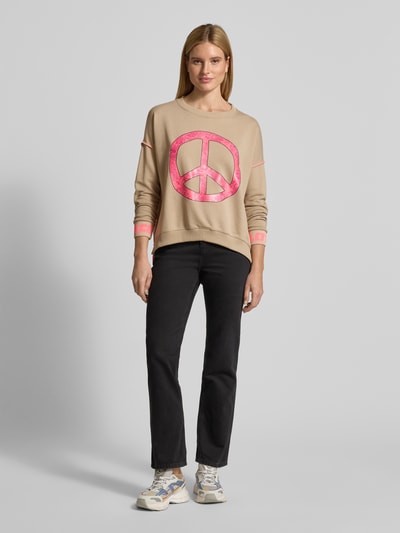 Modelka prezentuje Oversized Sweatshirt mit gerippten Abschlüssen von miss goodlife z bawełny, krój oversized, prążkowane wykończenia, okrągły dekolt, nadruk z motywem, kolor beżowy z różowym nadrukiem, całkowity widok z przodu