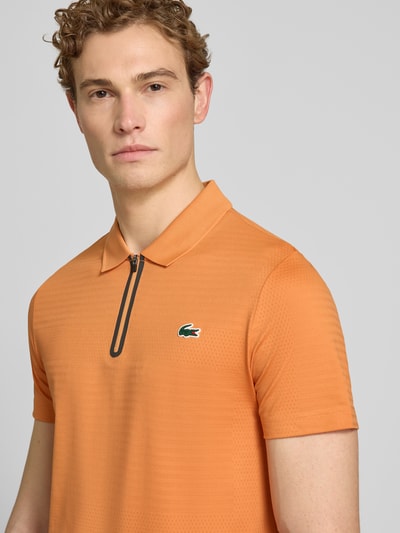 Männermodel trägt Slim Fit Poloshirt aus schnelltrocknendem Material von Lacoste, Optik: Unifarben, Logo-Patch, Nahaufnahme Oberkörper.