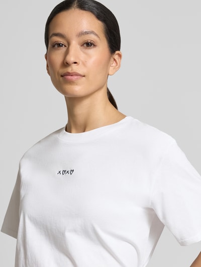 Modelka kobieca nosi Boxy Fit T-Shirt aus reiner Baumwolle von Tom Tailor Denim, biały, gładka faktura, haft z motywem, okrągły dekolt, krótkie rękawy, materiał typu cienki prążek, bawełna, zbliżenie na górną część ciała.