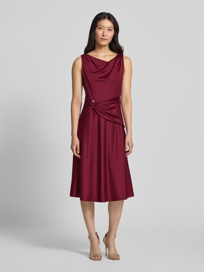 Frauenmodel trägt Cocktailkleid aus Satin mit Raffungen von Adrianna Papell in Bordeaux, taillierte Passform, Midilänge, Ganzkörperansicht von vorne.