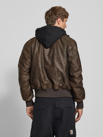 Männermodel trägt Bomberjacke in Leder-Optik mit Label-Details von Alpha Industries, dunkelbraune Farbe, Rückansicht, Ganzkörperansicht. Regular Fit, Kapuze, Stehkragen, Reißverschluss, Maße: Rückenlänge 63 cm, Schulterbreite 44 cm, Brustweite 52 cm, Ärmellänge 60 cm.