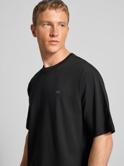 Männermodel trägt T-Shirt mit Label-Print von Levi's®, schwarze reine Baumwolle, lockerer Schnitt, gerippter Rundhalsausschnitt, Nahaufnahme Oberkörper.