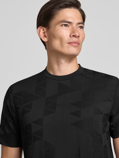 Männermodel trägt schwarzes Regular Fit T-Shirt aus reiner Baumwolle Modell 'TS_NETWORK JQ' von BOSS Green, geometrisches Muster, Nahaufnahme Oberkörper.
