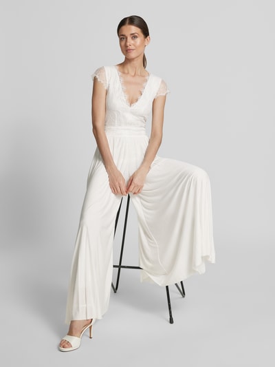 Vrouwenmodel draagt Braut-Jumpsuit met diepe V-hals model 'Emmie' van GUIDO MARIA KRETSCHMER WOMAN, rechte fit, wit, kanten top, plooibroek, tailleband, voorkant volledig lichaam.