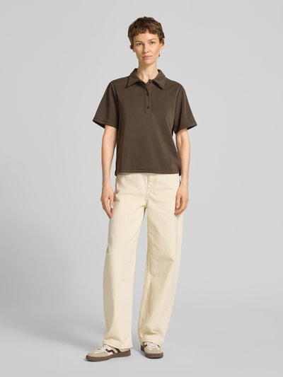 Kobiece model prezentuje koszulkę polo Loose Fit Poloshirt mit kurzer Knopfleiste Modell 'Helle' od My Essential Wardrobe, mieszanka materiałów z dodatkiem wiskozy, kołnierzyk polo, krótka listwa guzikowa, długość tyłu w rozmiarze S: 57 cm, widok całej sylwetki z przodu.