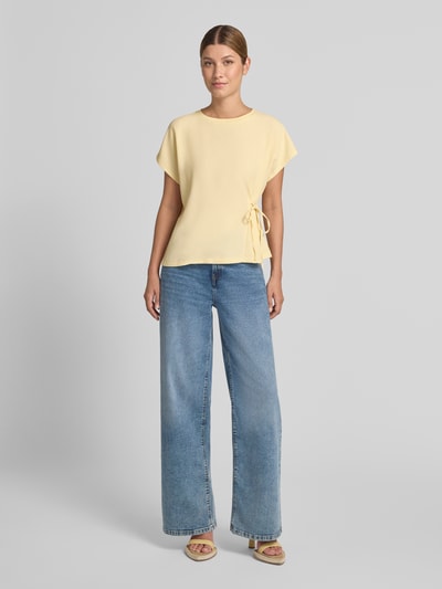 Frauenmodel trägt T-Shirt mit seitlicher Schnürung Modell 'Sifem' von OPUS in Hellgelb, kombiniert mit blauer Jeans, Ganzkörperansicht von vorne. Damen T-Shirt aus Viskose-Elasthan-Mix, Regular Fit, Rundhalsausschnitt, Rückenlänge bei Größe 36: 54 cm.