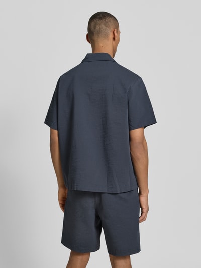 Mężczyzna model nosi Relaxed Fit Freizeithemd aus reiner Baumwolle von Lacoste w tkaninie stylizowanej na denim, krój relaxed fit, kołnierzyk koszulowy, listwa guzikowa na całej długości, naszywka z logo, rękaw: krótki, wykończenie materiału: marszczenie, materiał: bawełna; całkowity widok z tyłu