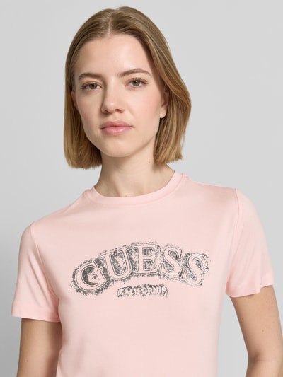 Modelka kobieca nosi T-Shirt aus Viskose-Elasthan-Mix mit Logo von Guess Activewear, jasnoróżowy kolor, krój regular fit, okrągły dekolt, długość tyłu w rozmiarze S: 53 cm, z widocznym logo, tekstura gładka, zbliżenie na górną część ciała