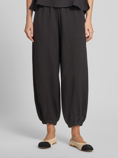 Vrouwenmodel draagt Relaxed Fit broek uit viscosemix model 'Myha' van OPUS, zwart met steekzakken, elastische band en boordjes, verkort, voorkant detailopname.