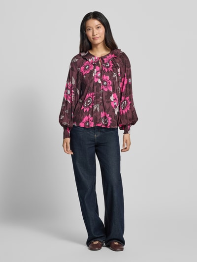 Frauenmodel trägt Relaxed Fit Bluse aus reiner Viskose von Christian Berg Woman, floraler Allover-Print in Pink und Braun, Umlegekragen, Langarm, Ganzkörperansicht von vorne.