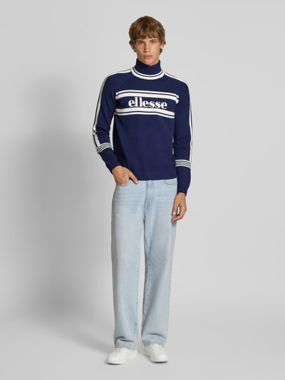 Männermodel trägt Turtleneck-Pullover aus Viskose-Mix Modell 'PELLINI' von Ellesse in Dunkelblau mit weißen Streifen, Ganzkörperansicht von vorne.