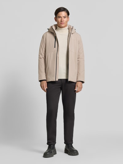 Männermodel trägt Regular Fit Jacke mit Logo-Print von Lindbergh aus elastyczna mieszanka materiałów, beż, Ganzkörperansicht von vorne. Kurtka, kaptur z tunelem, nadruk z logo, kieszeń napoleonka, Długość tyłu w rozmiarze M: 74 cm, szerokość ramion w rozmiarze M: 46 cm, szerokość klatki piersiowej w rozmiarze M: 42 cm, długość rękawów w rozmiarze M: 62 cm.