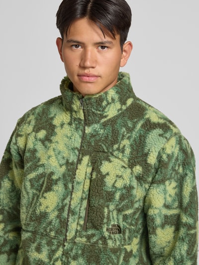 Männermodel trägt Fleecejacke mit Label-Stitching von The North Face in grüne camouflage Farben, borstzak met rits, recht model, opstaande kraag, borstzak, steekzakken aan de zijkant, ritssluiting, ruglengte maat M 67 cm, mouwlengte maat M 65 cm, Nahaufnahme Oberkörper