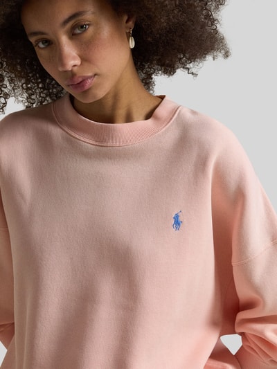 Modelka nosi Regular Fit Sweatshirt aus Baumwoll-Mix od Polo Ralph Lauren, jasnoróżowy, logo, okrągły dekolt, długie rękawy, bawełniany materiał, gładka faktura, ujęcie zbliżeniowe górnej części ciała.