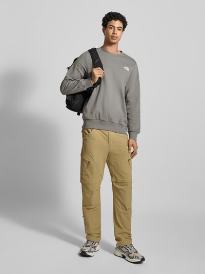 Mannelijk model draagt Sweatshirt mit Label-Print van The North Face in grijs, katoen, losse pasvorm, ronde hals, geribde boorden, volledige lichaamsvooraanzicht.