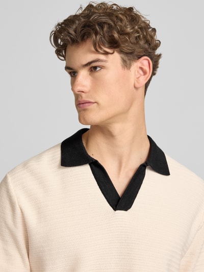 Männermodel trägt Regular Fit Poloshirt mit V-Ausschnitt Modell 'COTEDAZUR' von Jack & Jones aus Reine Baumwolle, Nahaufnahme Oberkörper. Rückenlänge bei Größe M: 67 cm, beigefarbene Struktur, schwarzer Kragen, Label-Detail.
